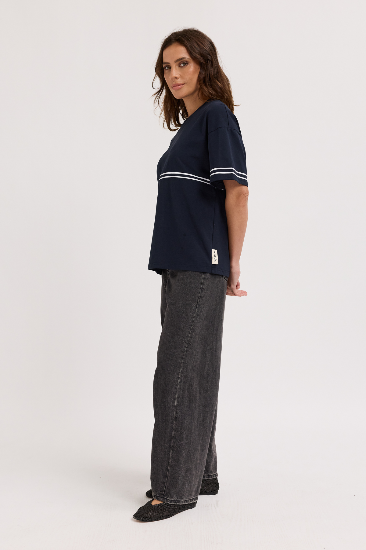 Woman wearing a navy blue t-shirt with white stripes and dark jeans on a white background