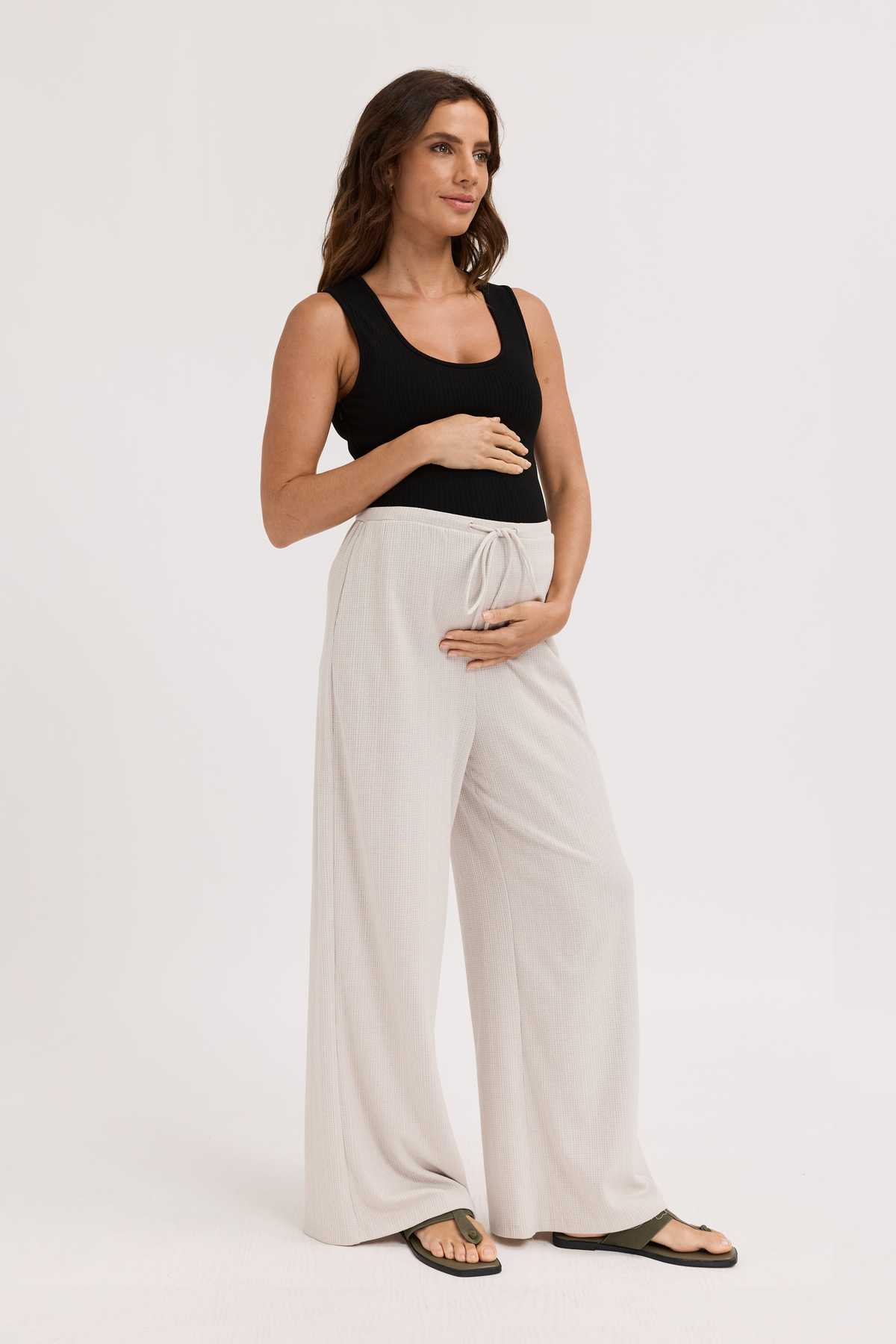 Woman wearing a black sleeveless top and light-colored wide-leg pants on a white background